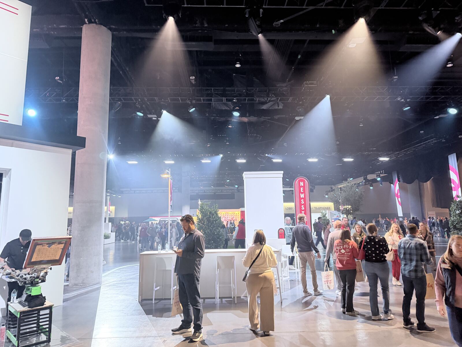 Large convention or trade show floor with a professional booth setup, dramatic stage lighting, and attendees walking through the illuminated space