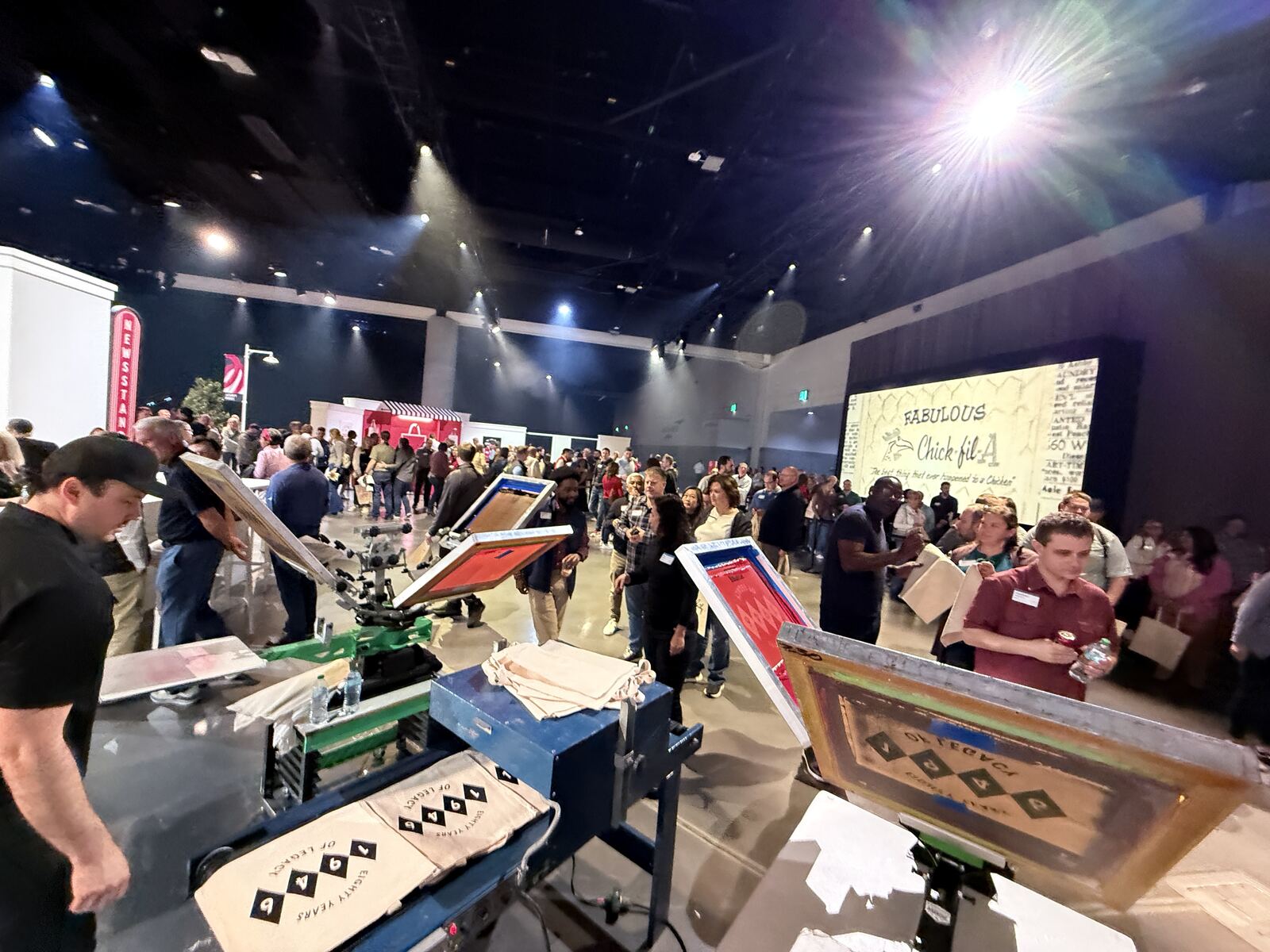 Large indoor event venue with multiple printing demo stations under professional stage lighting